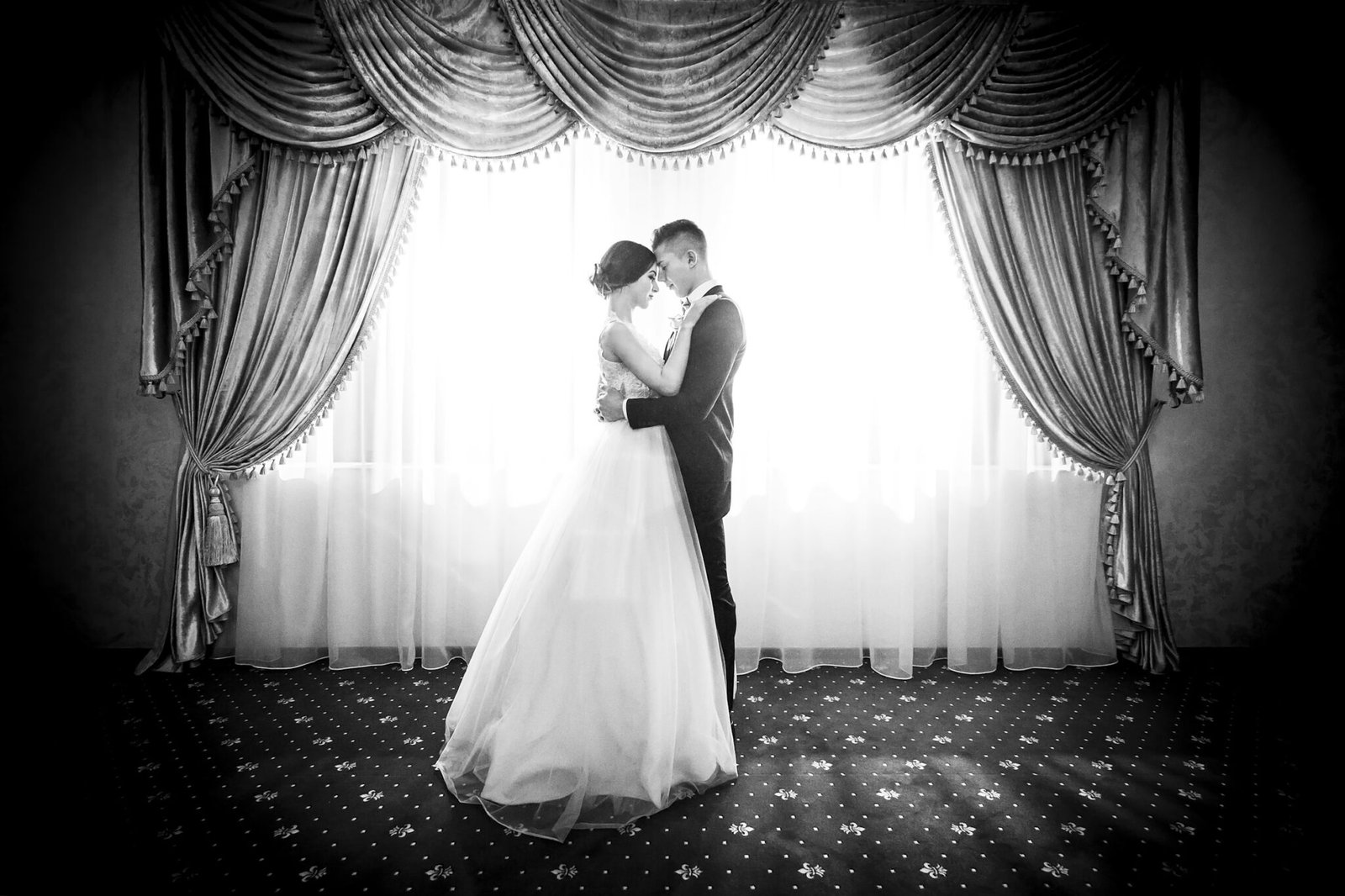 Black and white wedding portrait of a couple by a tall window